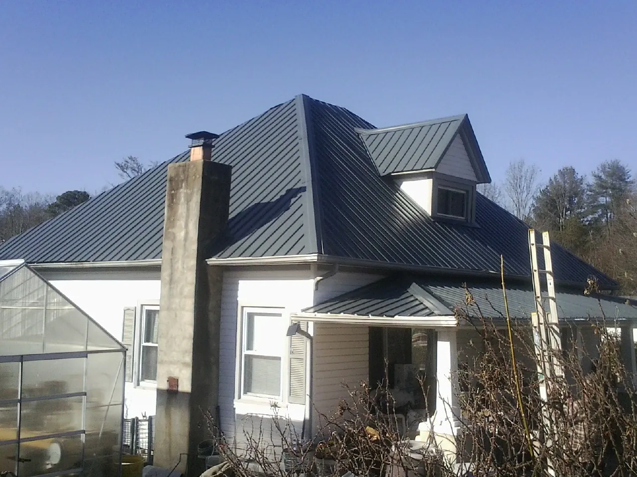 Dark blue standing seam metal roof on a white farmhouse with dormer — Slate & Tile Roof Repair by Roofing Brothers in Maple Park