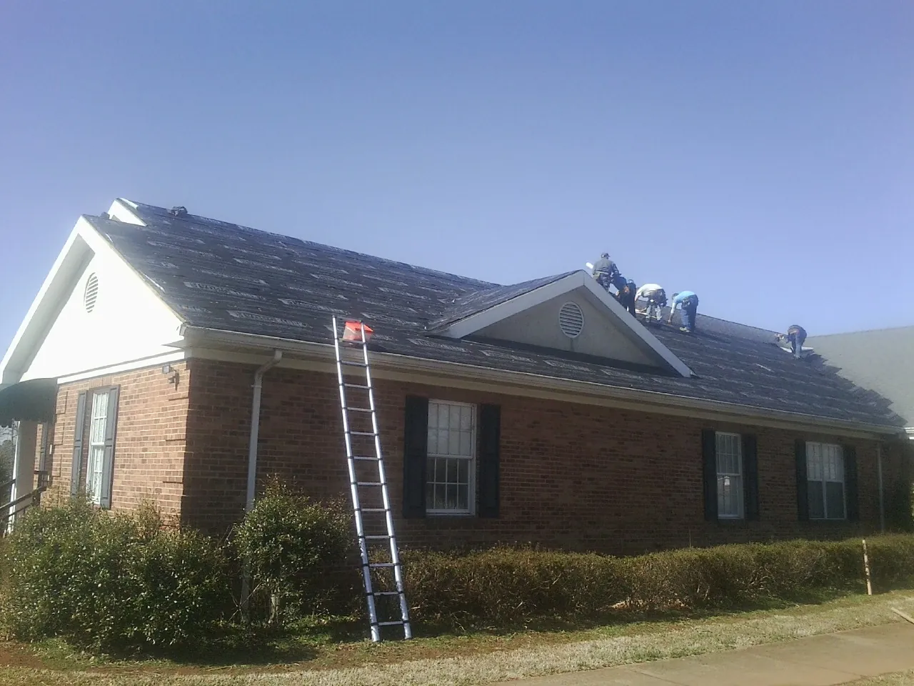 Crew tearing shingles off a brick ranch roof with a ladder set — Emergency Roof Repair work by our crew in Maple Park