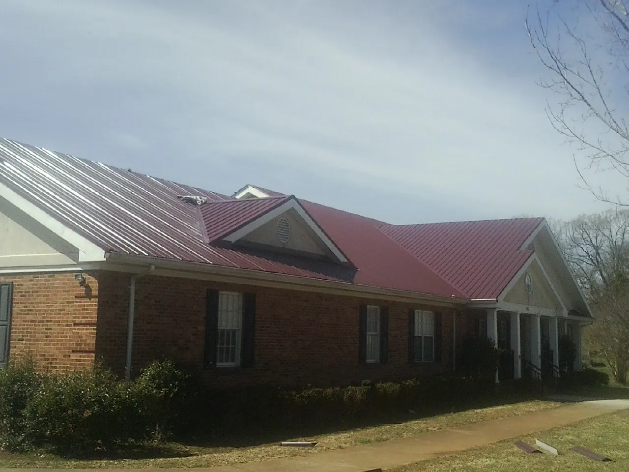 Red metal roof with gabled entries on a long brick building, from a Hail Damage Roof Repair job in Maple Park