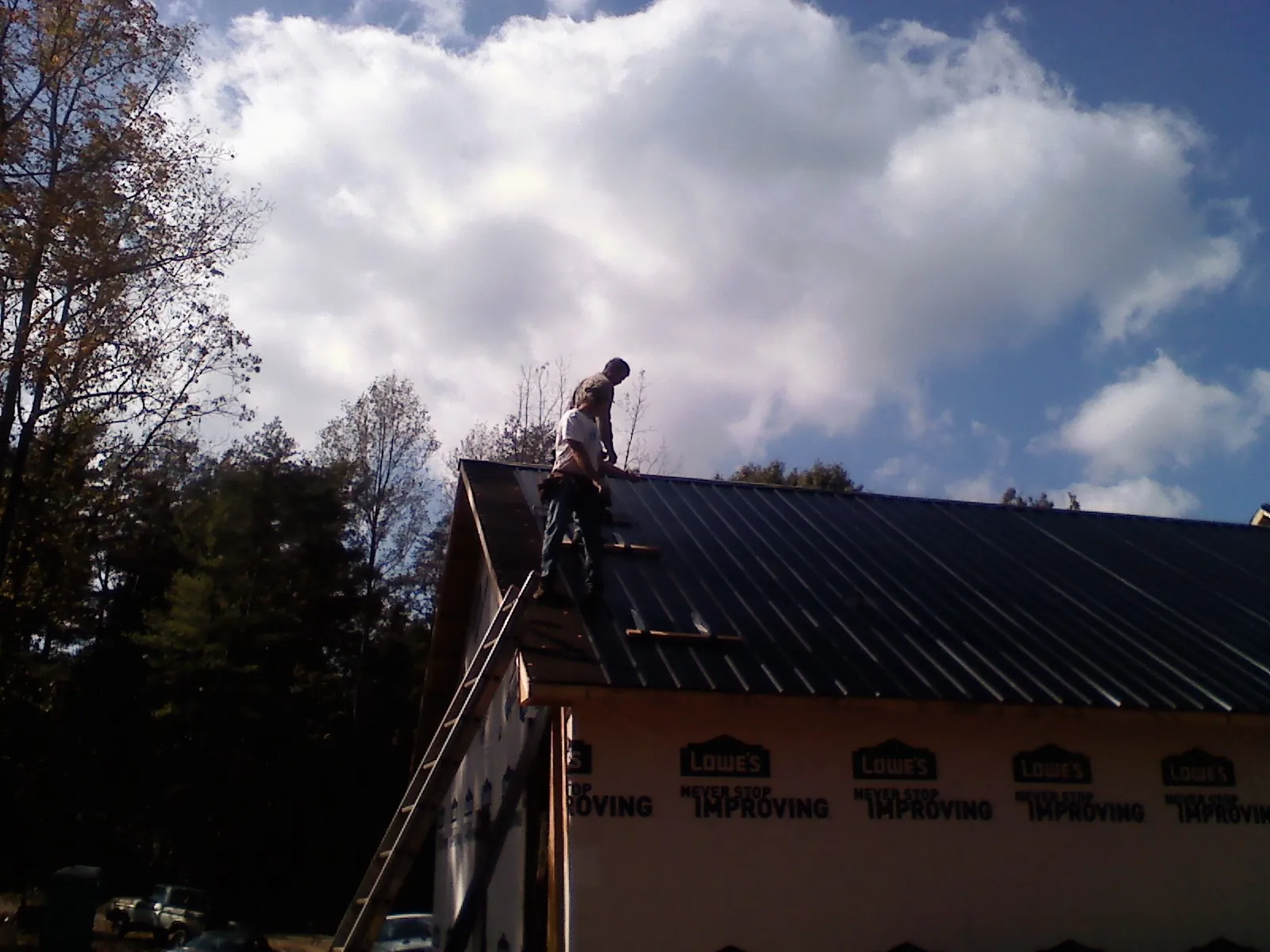Roofer fastening dark metal panels high against a cloudy sky, from a Roof Inspection job in Maple Park