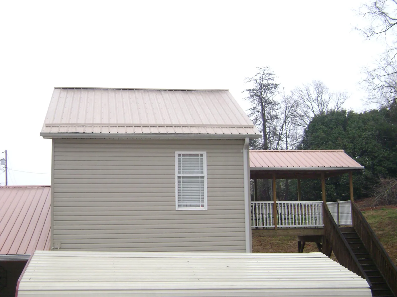 Tan metal roofs on a two story addition and attached porch, from a Roof Replacement job in Maple Park